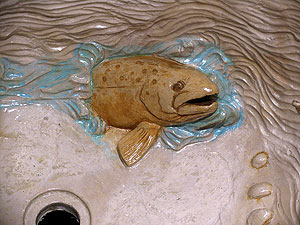 An upclose view of the fish that was carved into this concrete sink