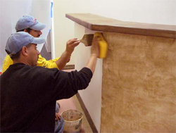 Workers apply Adobe Mirastain II to accent the sides of the front counter.