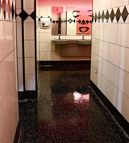Bathroom of 50s style diner white tiles with a band of black tiles and black epoxy floors.