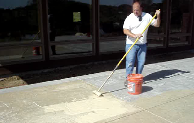 Applying the stain to the concrete with a roller and an orange 5 gallon bucket.