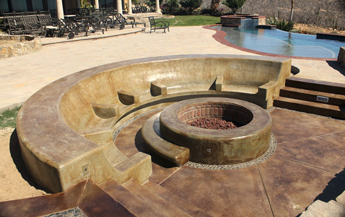 Circular acid stained concrete fire pit sits below deck