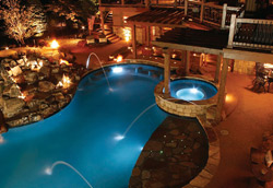 An aerial view of a pool lit at night with a reddish concrete pool deck.